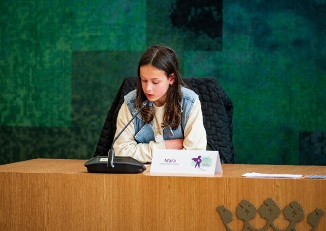 Kinderburgemeester Mara Staal zit in de raadszaal en spreekt in de microfoon.