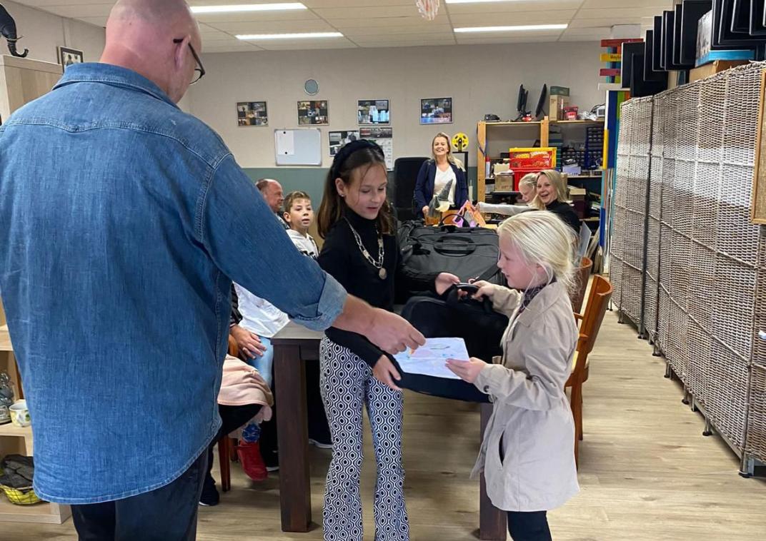 kinderburgemeester Mara Staal reikt een laptop uit aan een meisje. 
