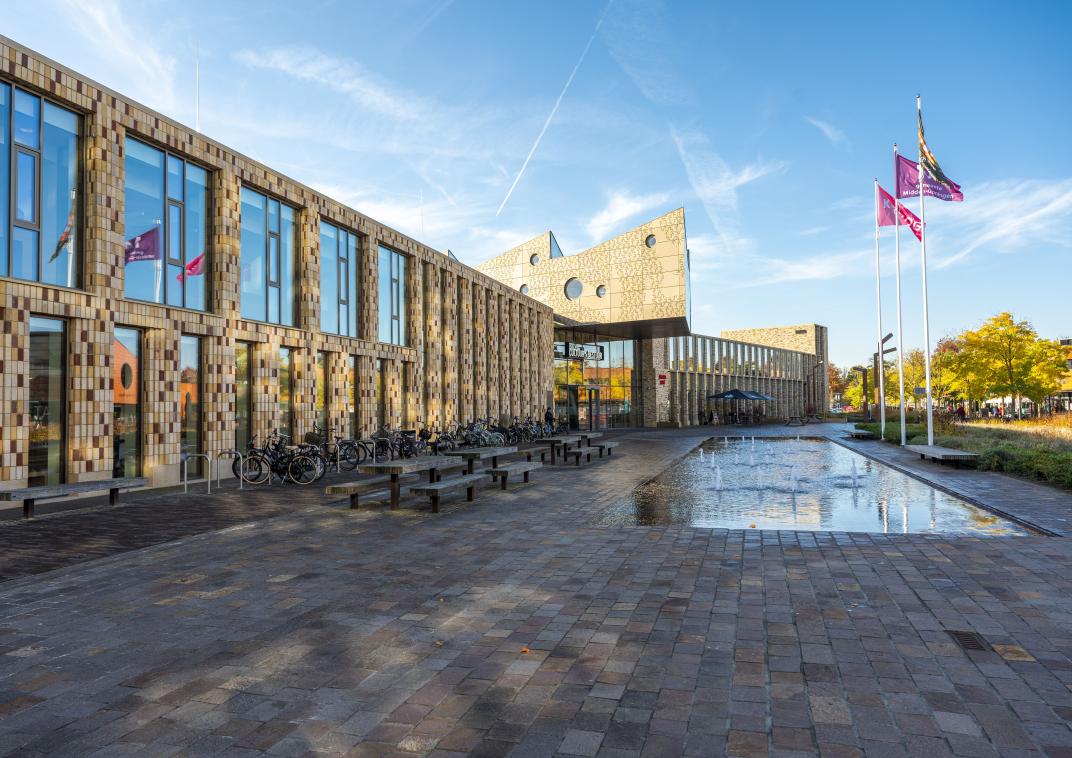 De voorkant van het Huis van Cultuur en Bestuur in Hoogezand. Voor het gebouw staan vlaggen en een fontein.