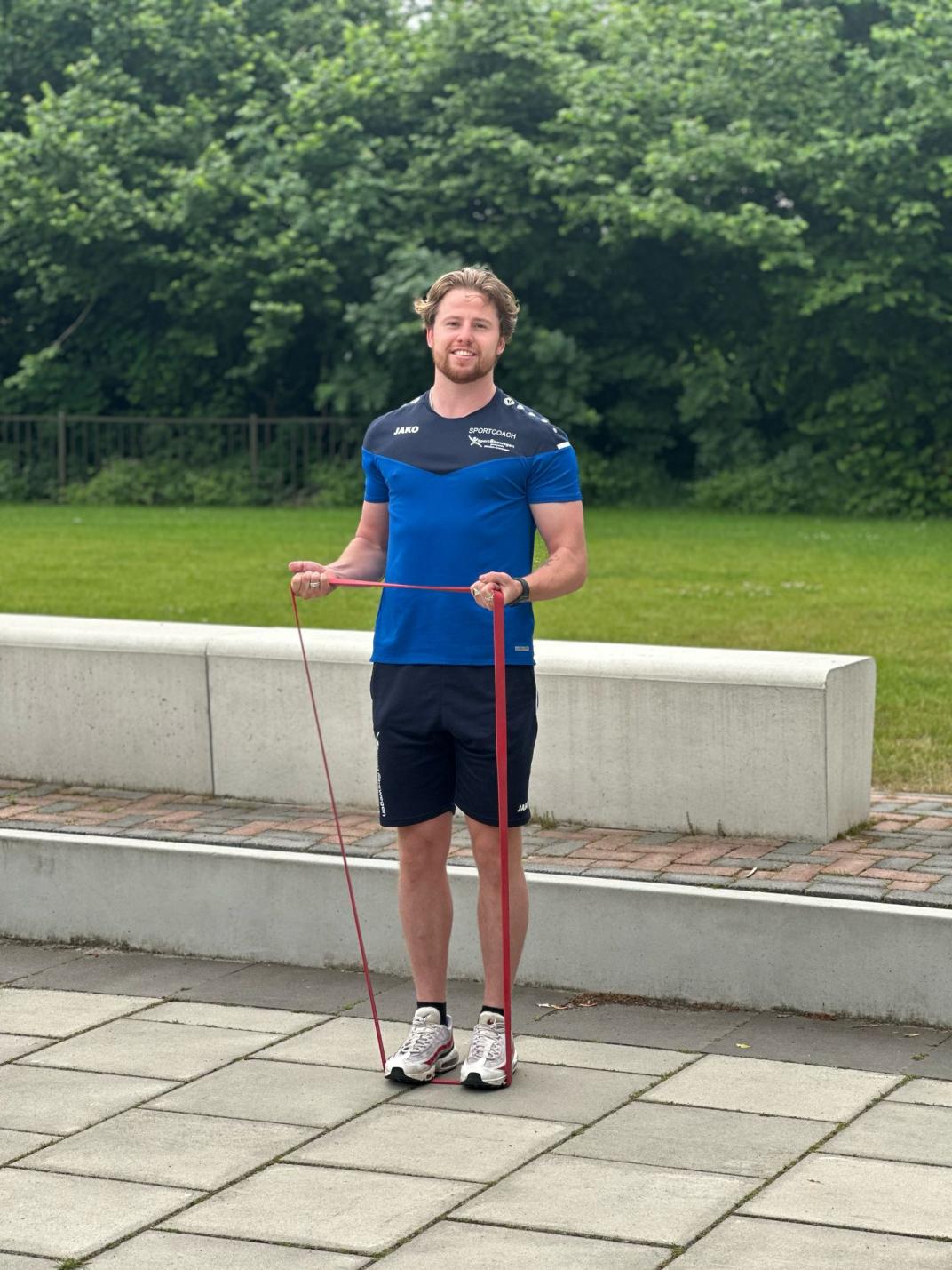 Lachende foto van sportcoach Mike die een oefening doet met een stretchband.