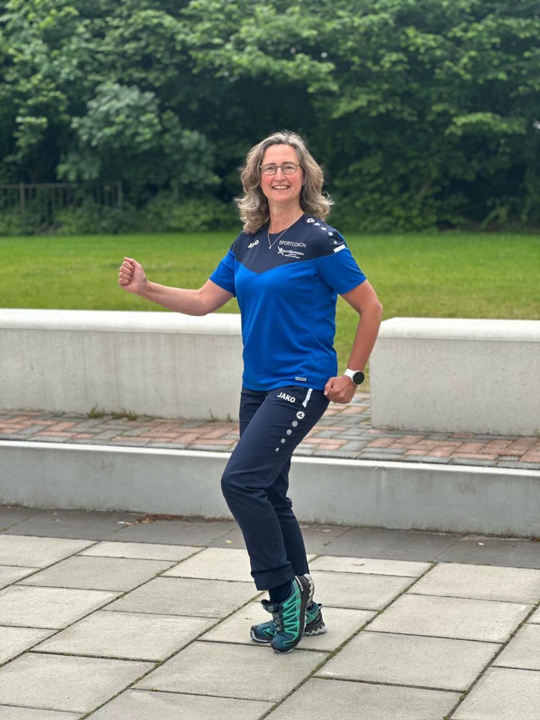 Lachende foto van sportcoach Petra die een hardloopbeweging uitbeeld.