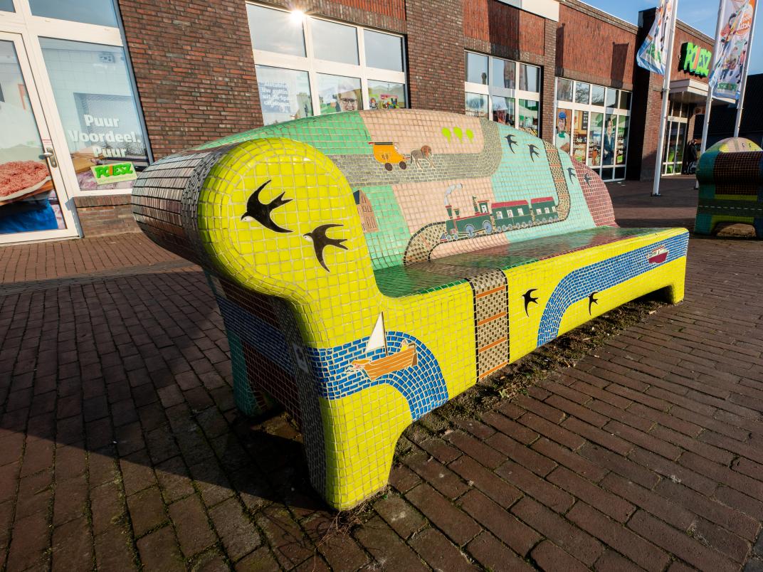 Foto van de Verhalenbanken in Zuidbroek. De bank is versierd met felgekleurde mozaïekstenen. 