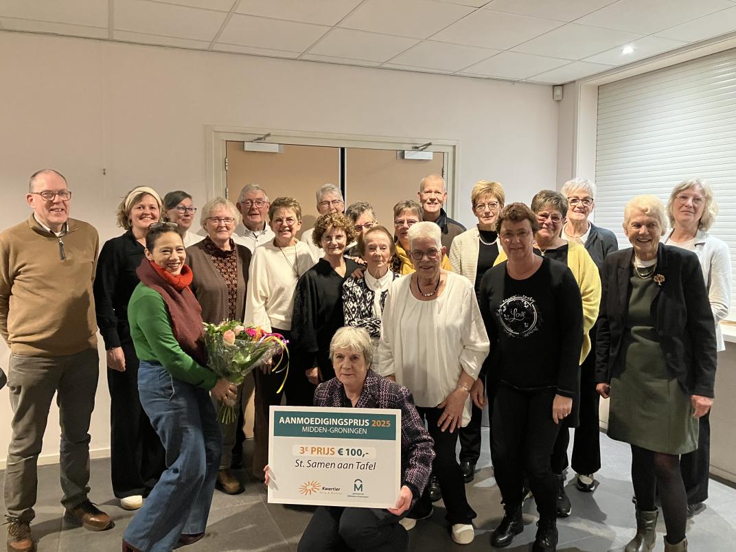 De vrijwilligers van Samen aan Tafel staan met zijn allen op de foto. Op de voorgrond is de prijs van 100 euro te zien.