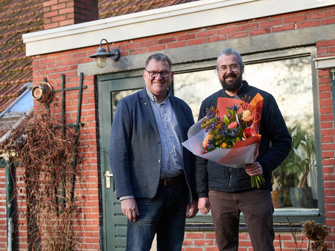 Wethouder Mellies verrast nieuwe bewoner Rico Zwaving met een bos bloemen voor zijn nieuwe huis in Noordbroek.