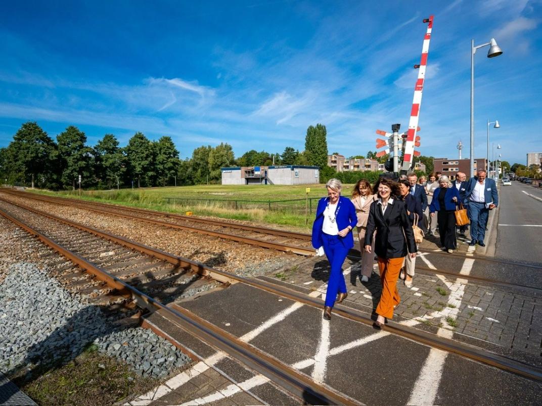 Burgemeester Erica van Lente, staatssecretaris Annet Bertram en andere partners die betrokken zijn bij de Nedersaksenlijn lopen over de spoorwegovergang aan de Kerkstraat in Hoogezand.