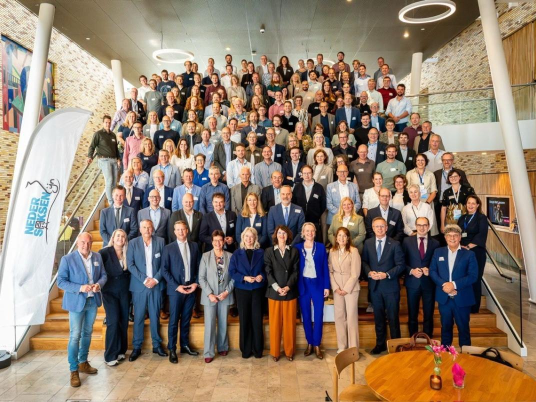 Groepsfoto betrokkenen Nedersaksenlijn in de centrale hal van het Huis van Cultuur en Bestuur in Hoogezand. In het midden staatssecretaris Annet Bertram en burgemeester Erica van Lente
