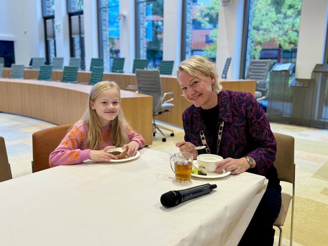 Een leerling van CBS de Wegwijzer zit aan tafel met burgemeester Erica van Lente. Samen eten ze hun ontbijt.