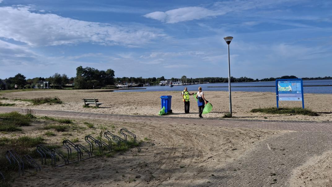 Twee mensen op het strand die afval aan het prikken zijn. 